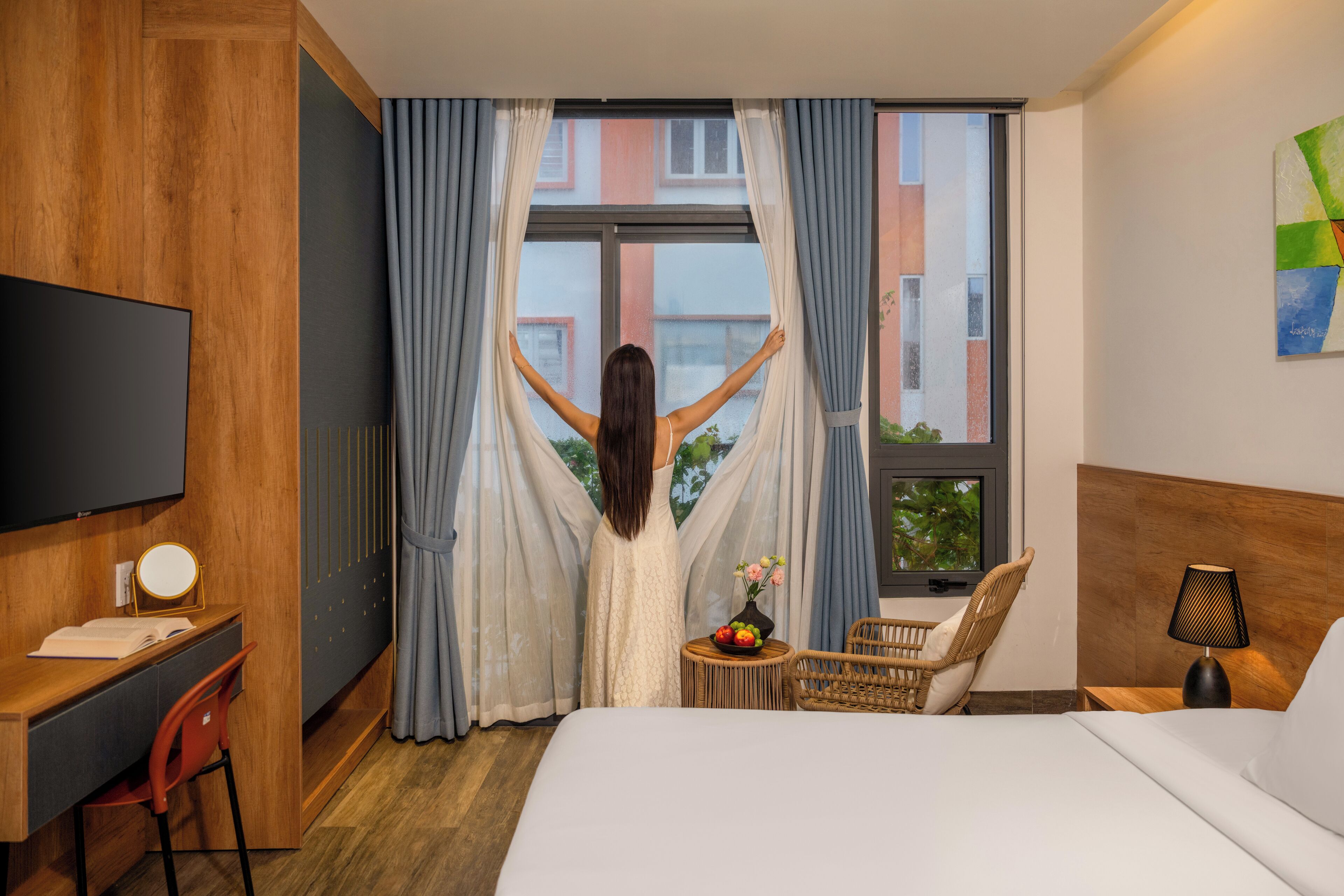 A hotel room with a bed, a desk, a chair, a TV, and a window with curtains.