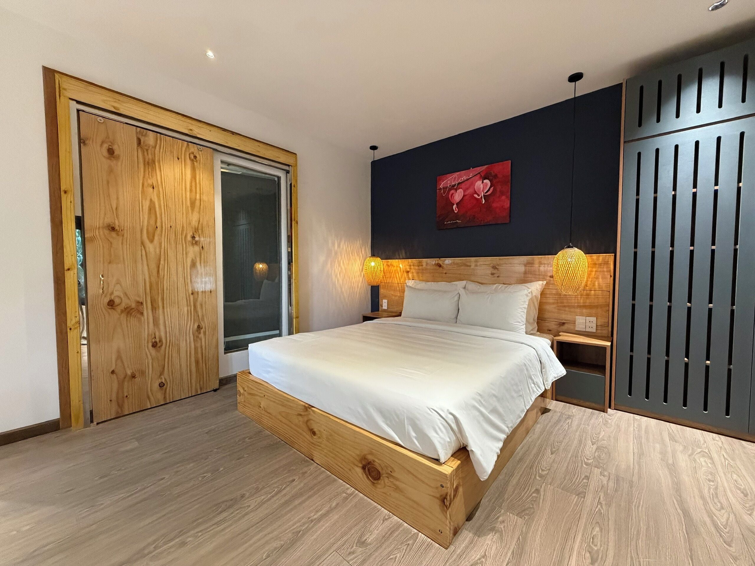 A bedroom with a wooden bed frame, a large window, and a dark wall with a red artwork.