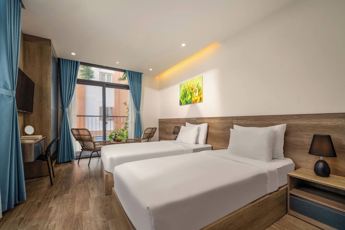 Ein Hotelzimmer mit zwei Betten, einem Schreibtisch, einem Sessel, einem Fernseher und einem Fenster mit Vorhängen.