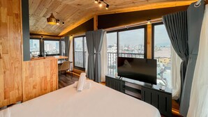 Une chambre d’hôtel avec un grand lit, une télévision, un bureau avec une chaise et une vue sur la ville grâce à de grandes fenêtres.