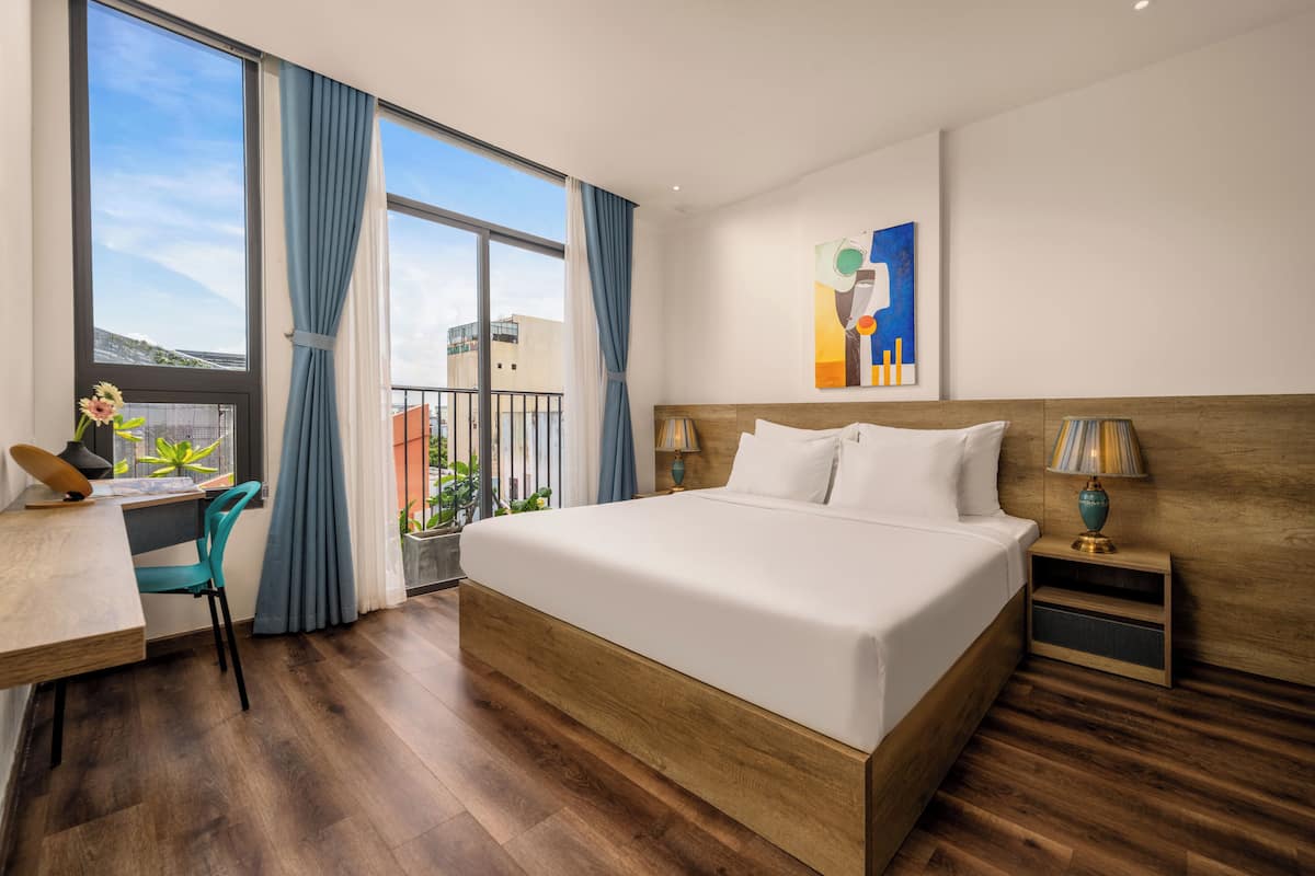 Ein Hotelzimmer mit einem großen Bett, einem Schreibtisch mit Stuhl, einem Fenster mit Vorhängen und einem Gemälde an der Wand.