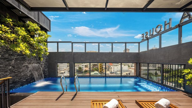 Une piscine sur le toit offrant une vue dégagée sur la ville, une terrasse en bois et des chaises longues avec des serviettes.