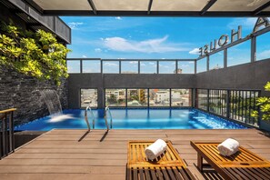 A rooftop pool with a clear view of the cityscape, a waterfall feature, and lounge chairs with towels. - Lantana House Boutique Da Nang (Da Nang)