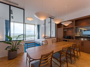 Ein modernes Hotelzimmer mit einem großen Esstisch, Holzstühlen, einem Blumentopf und Meerblick.