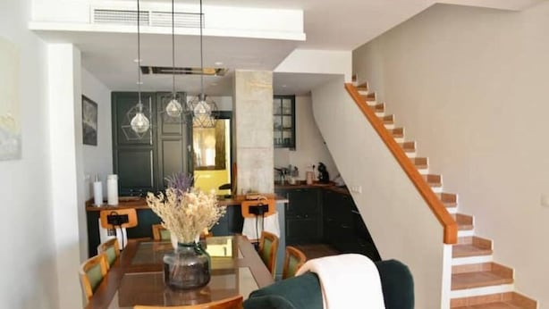 A dining area with a wooden table, chairs, and hanging pendant lights. A staircase with wooden steps leads to an upper floor. - Atenas Jávea (Jávea)