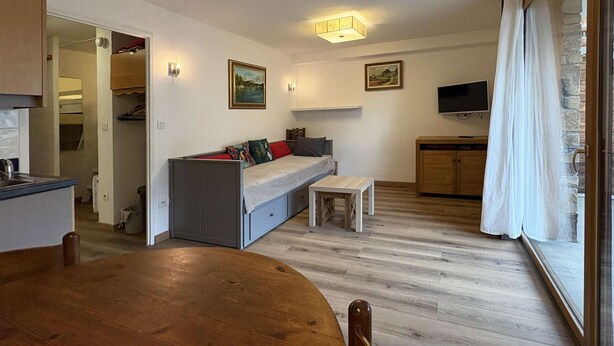 A compact living space with a kitchenette, a dining area, a sofa with cushions, a small table, and a TV mounted on the wall. - Ski-In/Ski-Out Studio with Pool Access at Les Orres 1800 (Les Orres)