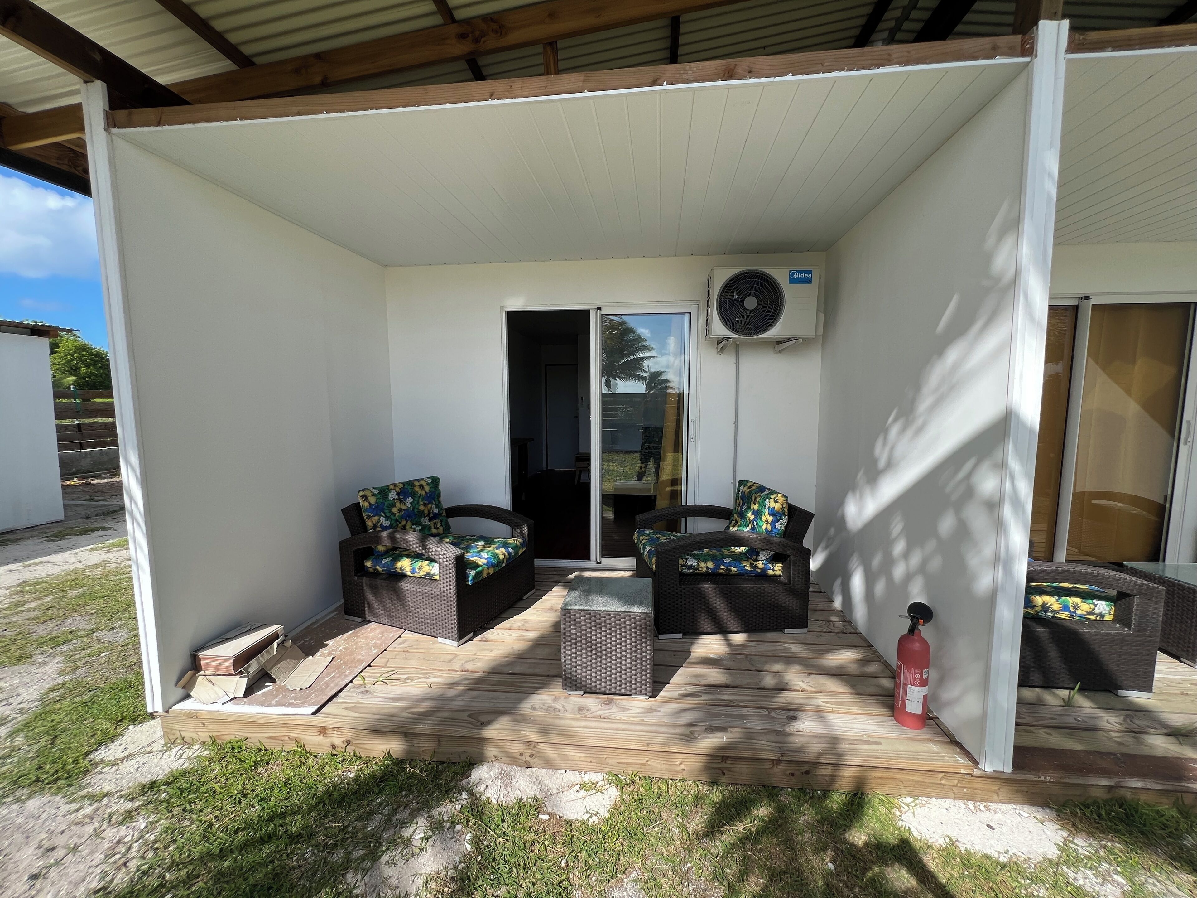 A covered patio area with two wicker sofas and cushions, a fire extinguisher, and an air conditioning unit.