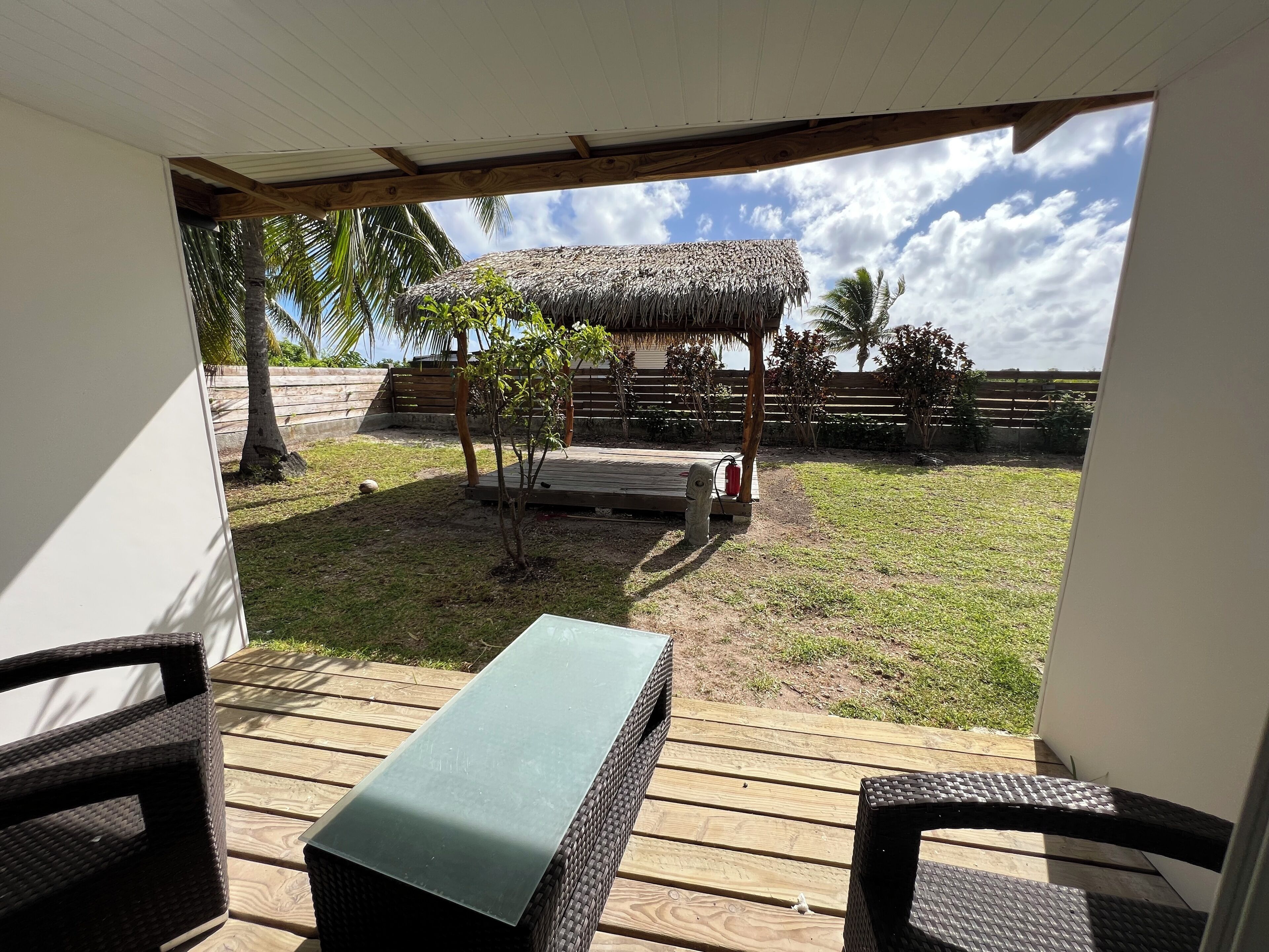 Une terrasse extérieure aménagée avec des meubles en osier, une structure dotée d’un toit de chaume et un espace verdoyant agrémenté de palmiers.