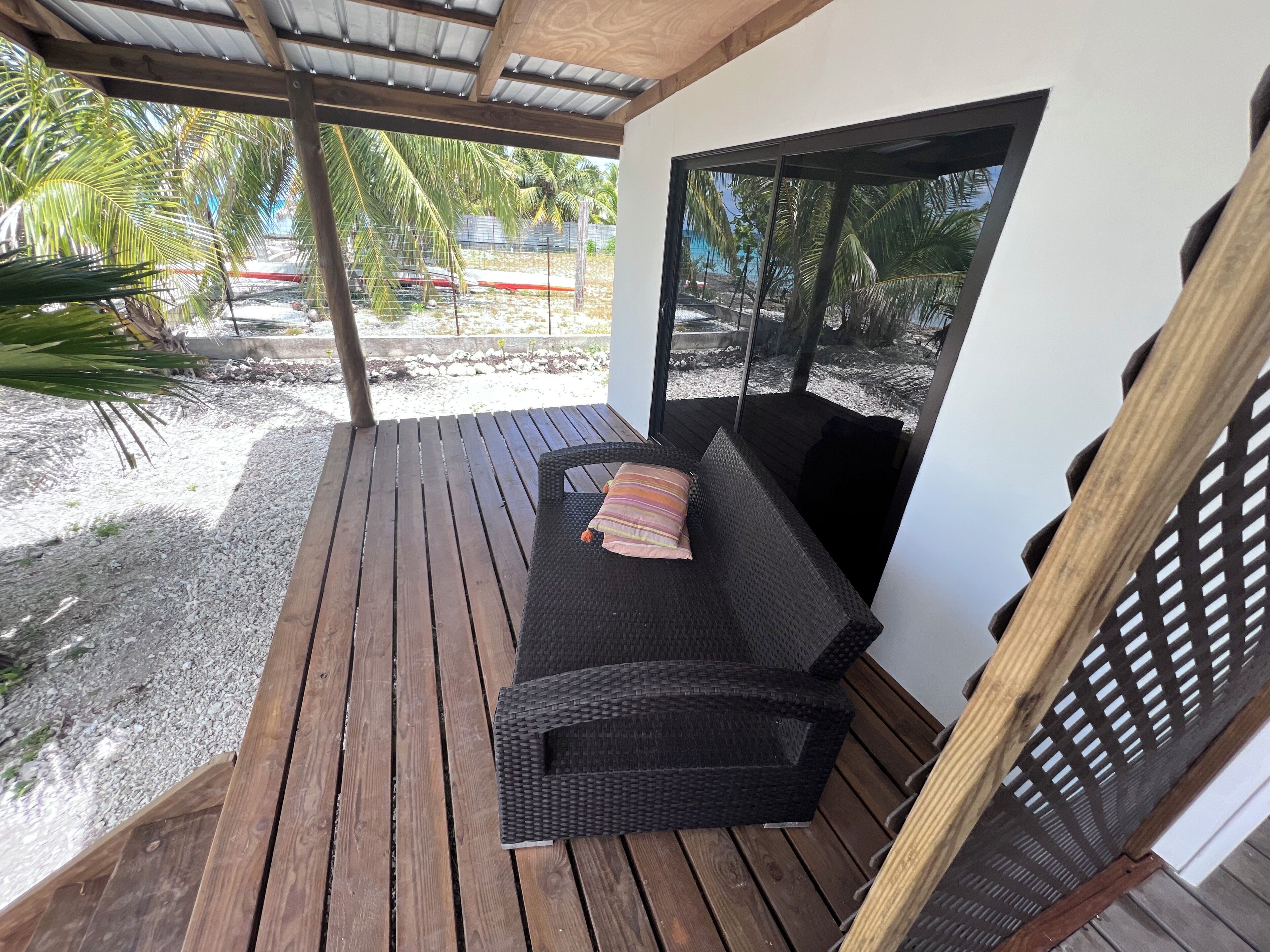 A covered outdoor seating area with a wicker sofa and a wooden bench.