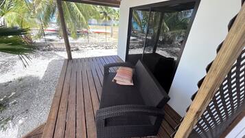 A covered outdoor seating area with a wicker sofa and a wooden bench.