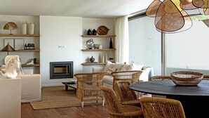 A modern living room with a fireplace, wicker furniture, and a large window. - Luxury Beach Villa - Casa do Forte- Infinity pool. (Albufeira)