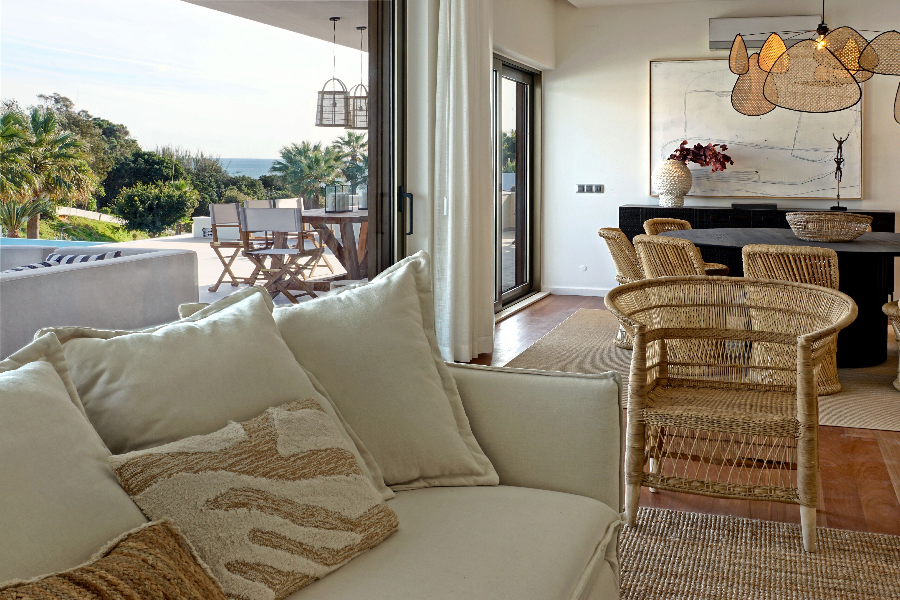 Een moderne woonkamer met een bank, rieten stoelen, een eethoek en uitzicht op zee.