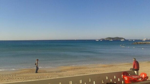 Ein Strand mit blauem Himmel, sandigem Ufer und ein paar Booten im Wasser.