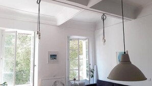 Ein Zimmer mit großen Fenstern, einer Couch, einem Tisch und Pendelleuchten.