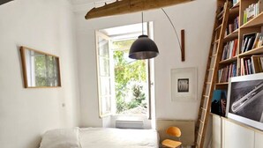 Ein Schlafzimmer mit Bett, Stuhl, Bücherregal und Fenster.