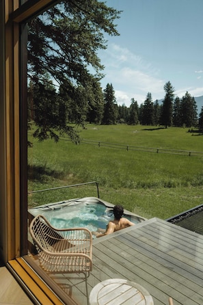 A hot tub on a wooden deck with a view of a grassy field and trees.