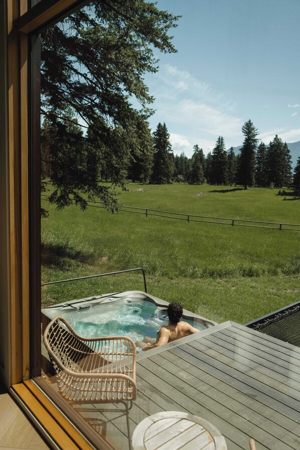 A hot tub on a wooden deck with a view of a grassy field and trees. - Getaway - Cozy Montana Escape (Columbia Falls)