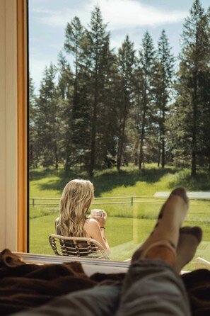 A person seated by a window with a view of a forest and a lake.