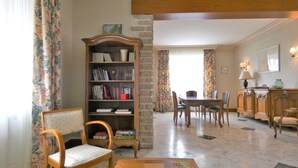 Ein Zimmer mit einer Holzbücherwand, einem Esstisch mit Stühlen und einem gemusterten Teppich.