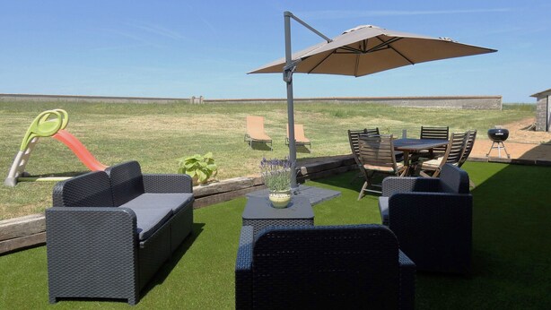 Ein Terrassenbereich im Freien mit Korbmöbeln, einem Tisch und einem Sonnenschirm.