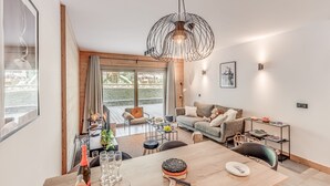 A modern living room with a wooden dining table, a sofa, and a large window overlooking a deck.