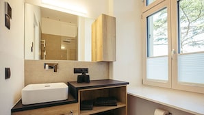 A modern bathroom with a large mirror, a sink, a vanity, and a window with blinds.