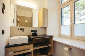 Une salle de bain moderne avec un grand miroir, un lavabo, un meuble-vasque et une fenêtre équipée de stores.
