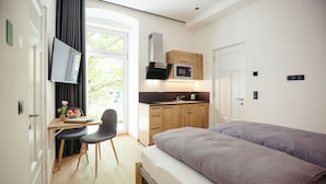 A modern bedroom with a bed, a desk, a chair, a TV, and a kitchenette.