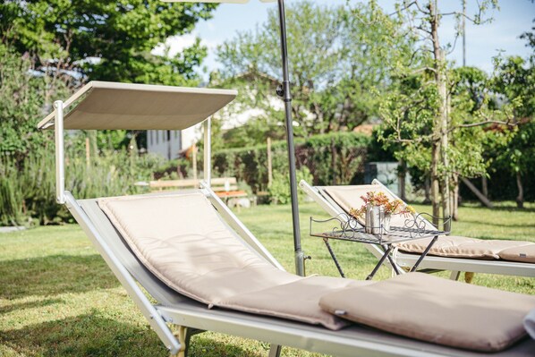 Deux fauteuils de jardin avec des auvents intégrés, une petite table ornée d’un vase de fleurs et un espace jardin avec pelouse.