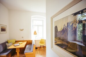Une pièce avec une table en bois, une chaise jaune, un canapé et un tableau encadré accroché au mur.