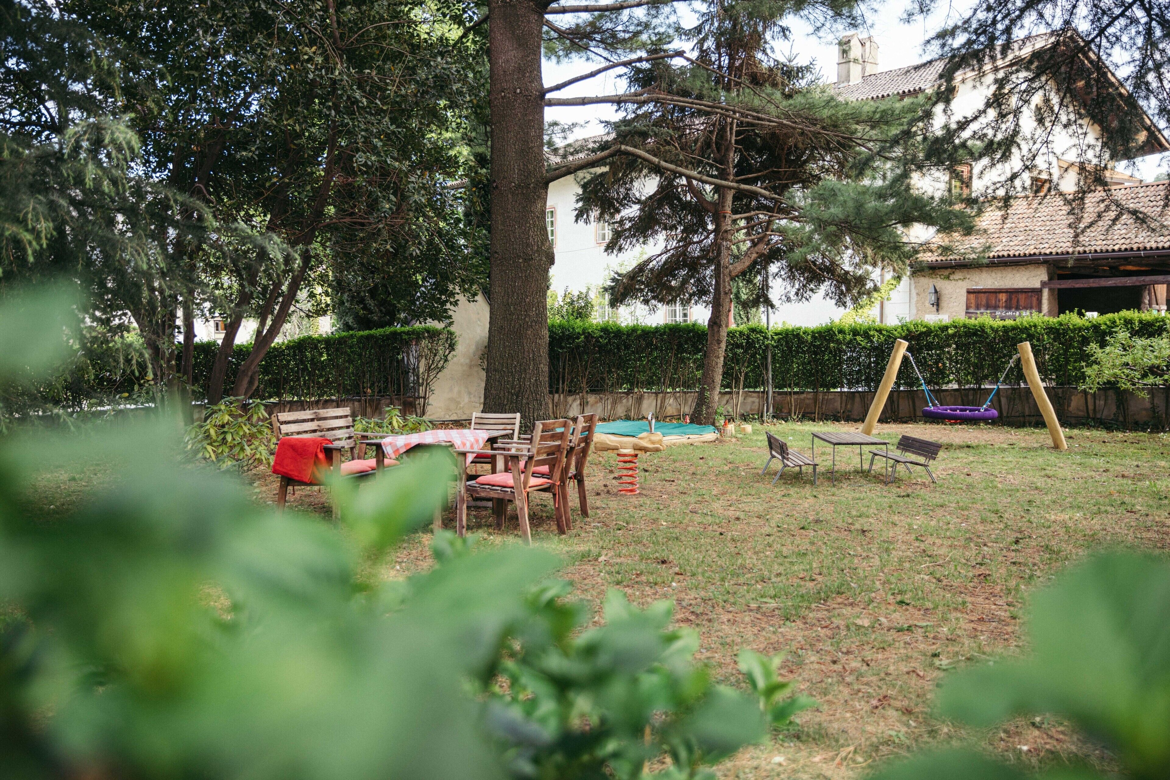 Patio trasero con mesa y sillas de madera, un columpio y un seto.