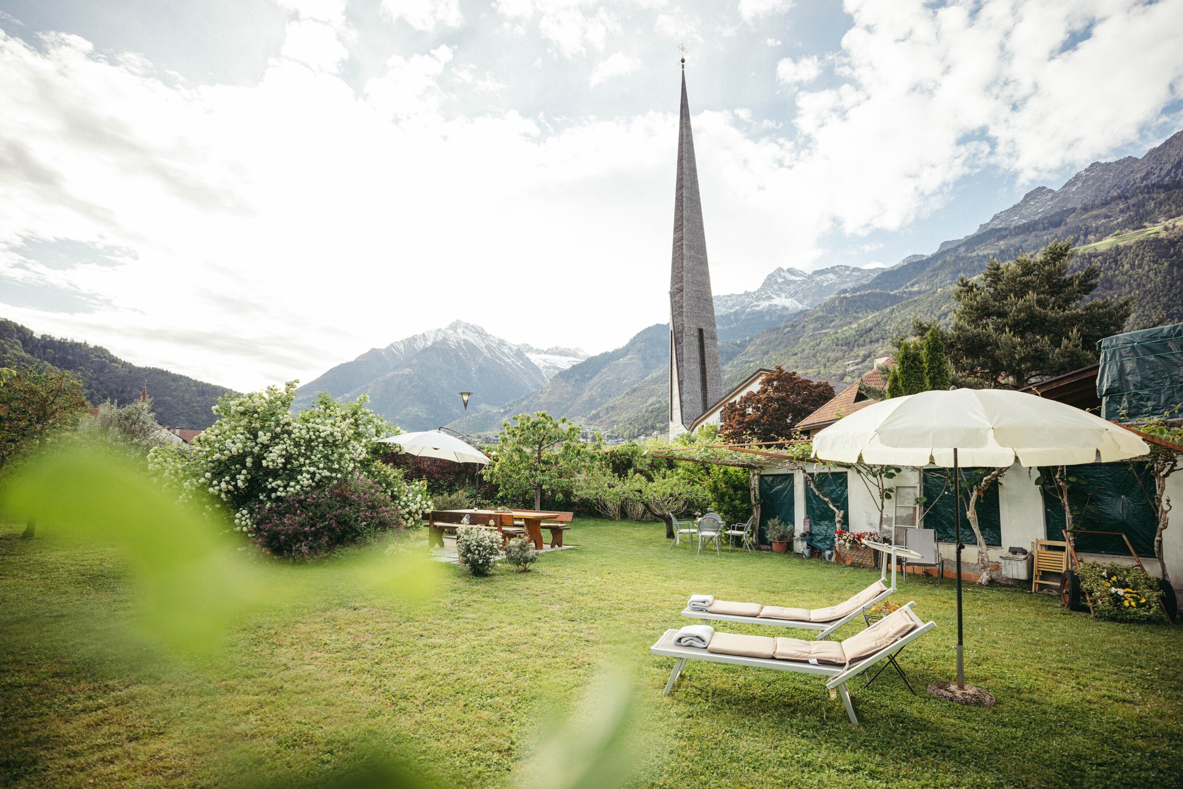 A garden with lounge chairs, a table, and umbrellas, with mountains in the background.