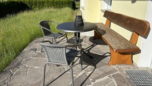 Eine Terrasse im Freien mit einem runden Tisch, zwei Stühlen und einer Holzbank.