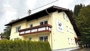 Ein zweistöckiges Gebäude mit gelber Fassade, einem Balkon mit Holzgeländern und einem Schild, das es als Wohnkomplex kennzeichnet.