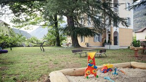 Un’area giochi sabbiosa con giochi, una panchina e un edificio con un balcone sullo sfondo.