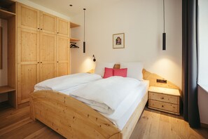 A wooden bed with white bedding, a nightstand, a wooden wardrobe, and a wall-mounted picture.
