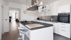 A modern kitchen with white cabinetry, a central island with bar stools, a built-in oven, and a stainless steel range hood.