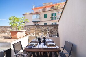 An outdoor dining area with a table set for two, surrounded by stone walls and a building with balconies. - La Cala Terrace by Domusicily (Palermo)