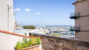 A balcony with a stone wall, a potted plant, and a view of a marina with boats.