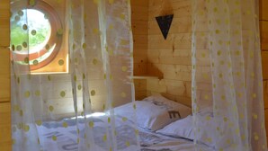 Una habitación de cabaña de madera con una cama, una ventana con vistas y una cortina con lunares amarillos.