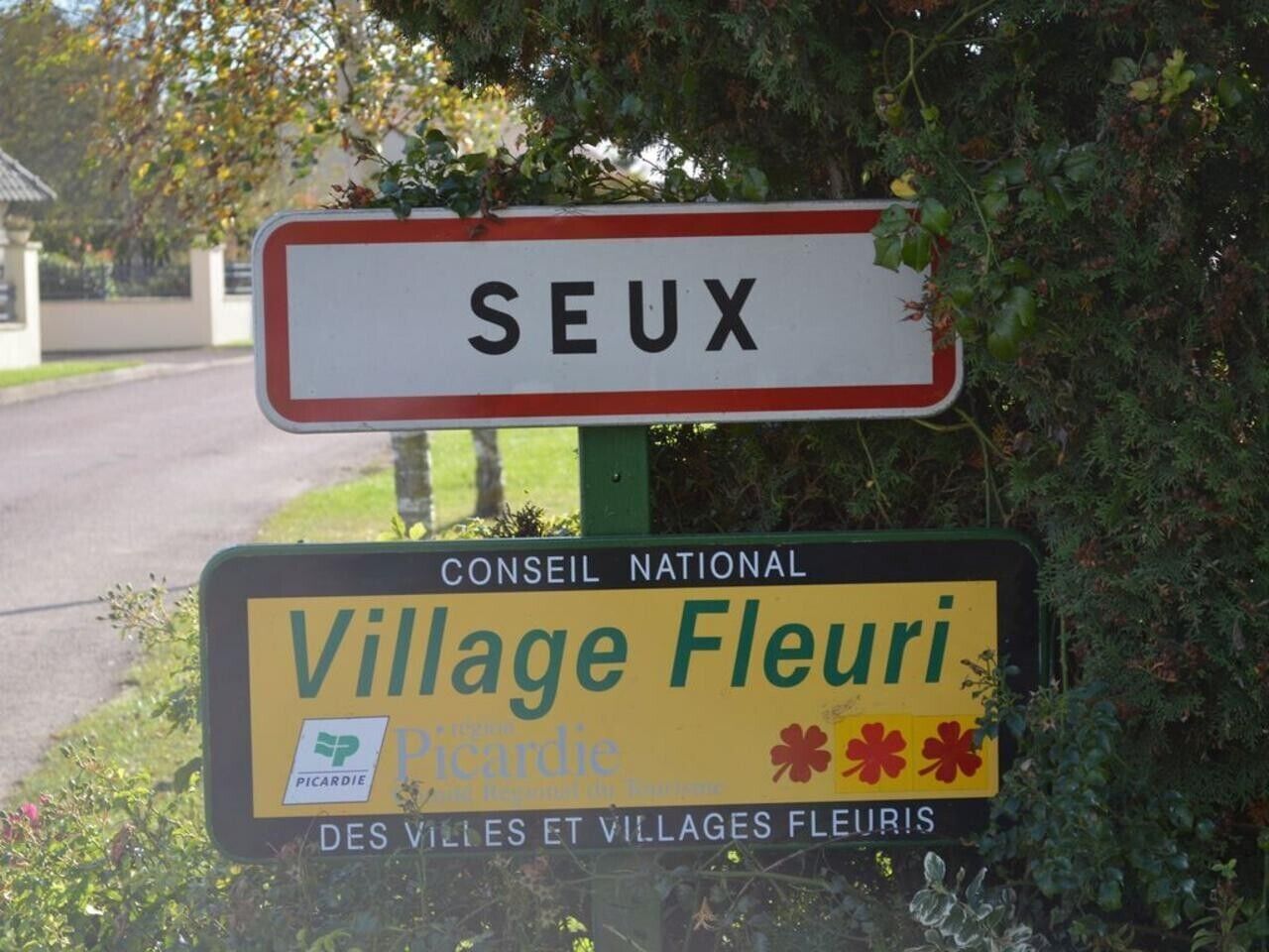 Un cartello con la scritta 'SEUX' e 'Village Fleuri', che indica un luogo.