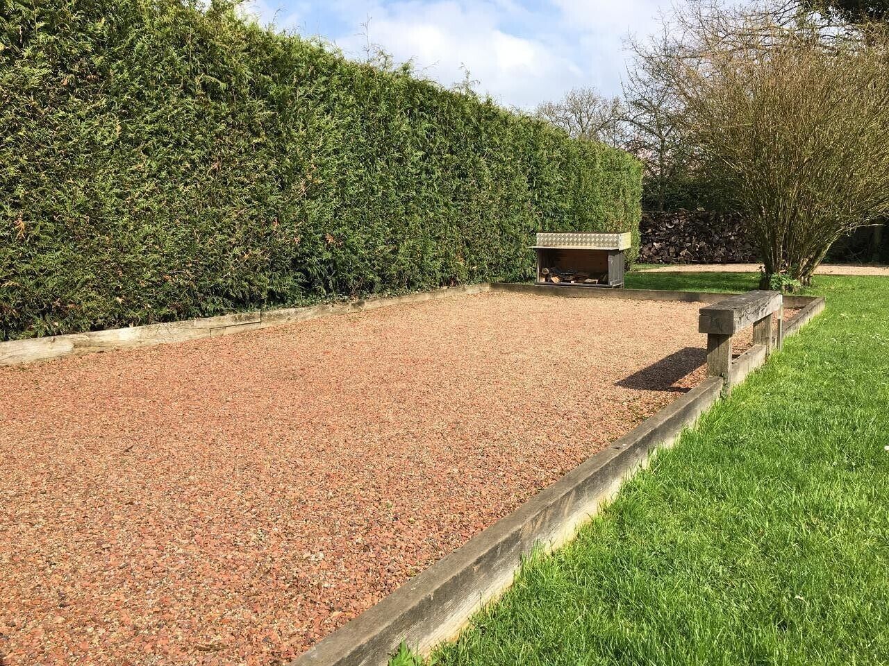 A gravel area with a wooden bench, a small structure, and a hedge.