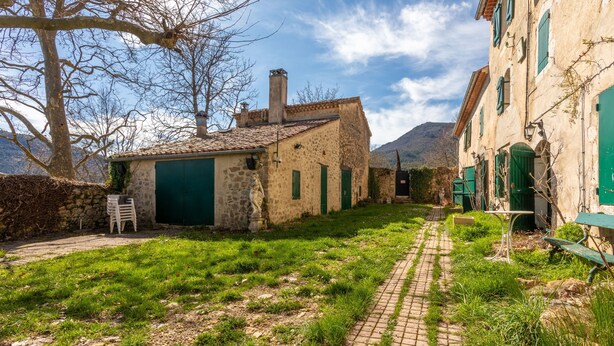 A narrow cobblestone path leading to a stone building with a green door, surrounded by greenery and mountains in the background. - Holiday Home 'Véritable Mas Provençal À La Palud' with Private Garden and Wi-Fi (La Palud-sur-Verdon)