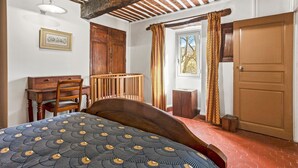 A bedroom with a wooden bed, a desk, a chair, a window with curtains, and a door. - Holiday Home 'Véritable Mas Provençal À La Palud' with Private Garden and Wi-Fi (La Palud-sur-Verdon)