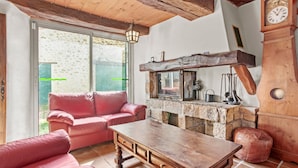 A cozy room with a stone fireplace, a wooden table, a pink sofa, and a clock on the wall. - Holiday Home 'Véritable Mas Provençal À La Palud' with Private Garden and Wi-Fi (La Palud-sur-Verdon)