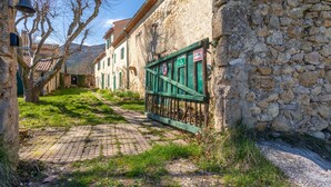 A narrow cobblestone street with stone buildings, a green gate, and a bell. - Holiday Home 'Véritable Mas Provençal À La Palud' with Private Garden and Wi-Fi (La Palud-sur-Verdon)