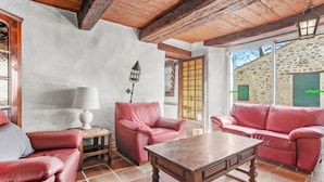 A room with a wooden ceiling, a stone wall, a red leather sofa, a wooden table, and a lamp. - Holiday Home 'Véritable Mas Provençal À La Palud' with Private Garden and Wi-Fi (La Palud-sur-Verdon)