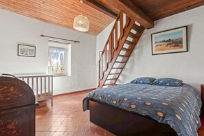A bedroom with a bed, a wooden staircase, a window, and a picture on the wall.
