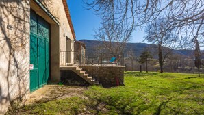 Um edifício de pedra com uma porta verde, uma escadaria que dá para um balcão e um gramado.