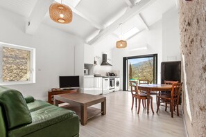 A modern kitchen with white appliances, a dining area with wooden furniture, and a large window offering a view.